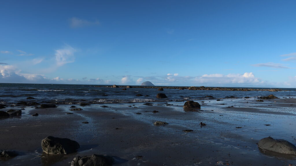 Sandy shore with boulders, rocky isle and the island Ailsa Craig in the background