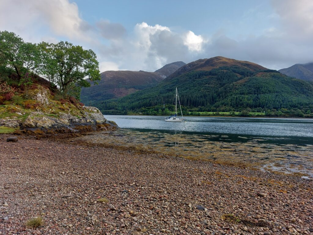 Bishop's Bay, with pebble shore, rocky headland and sailboat in the water