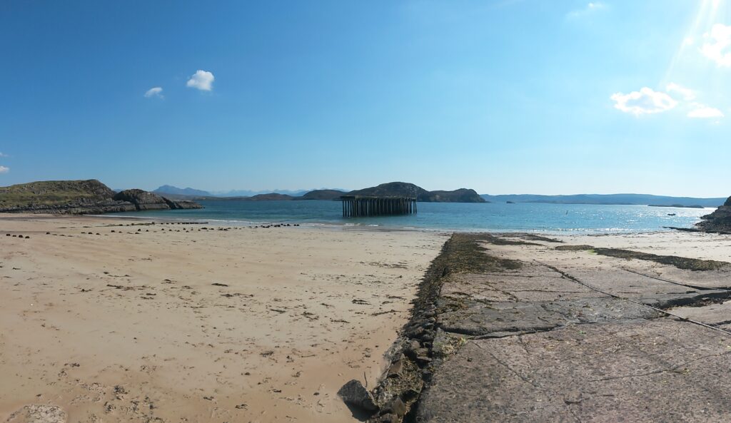 Sandy shore of Mellon Charles. Submerged in the water within the middle of the bay is an old WWII pier.